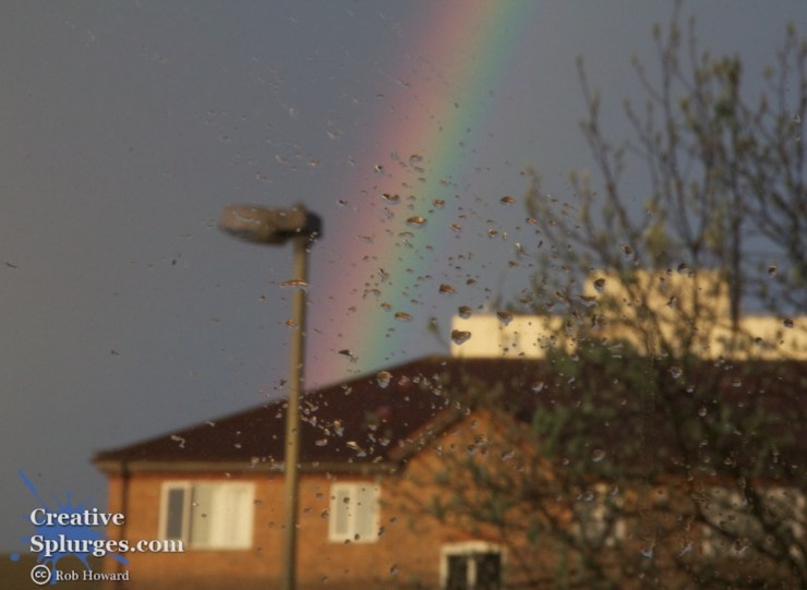Droplets of water on a window, with a lamppost and rainbow in the background
