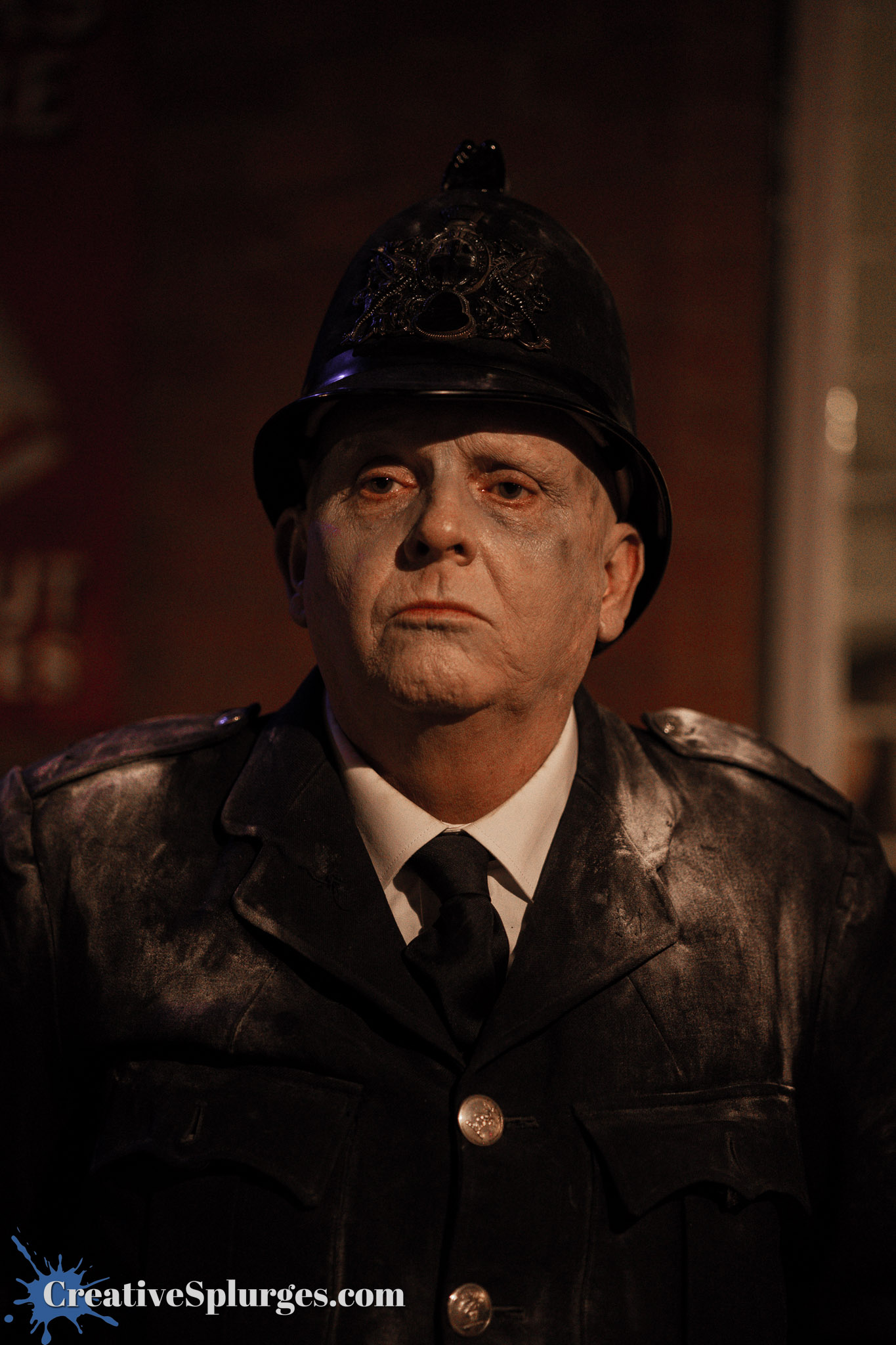 A man dressed as a vintage police officer, wearing a black helmet and coat, with a serious expression and pale makeup.