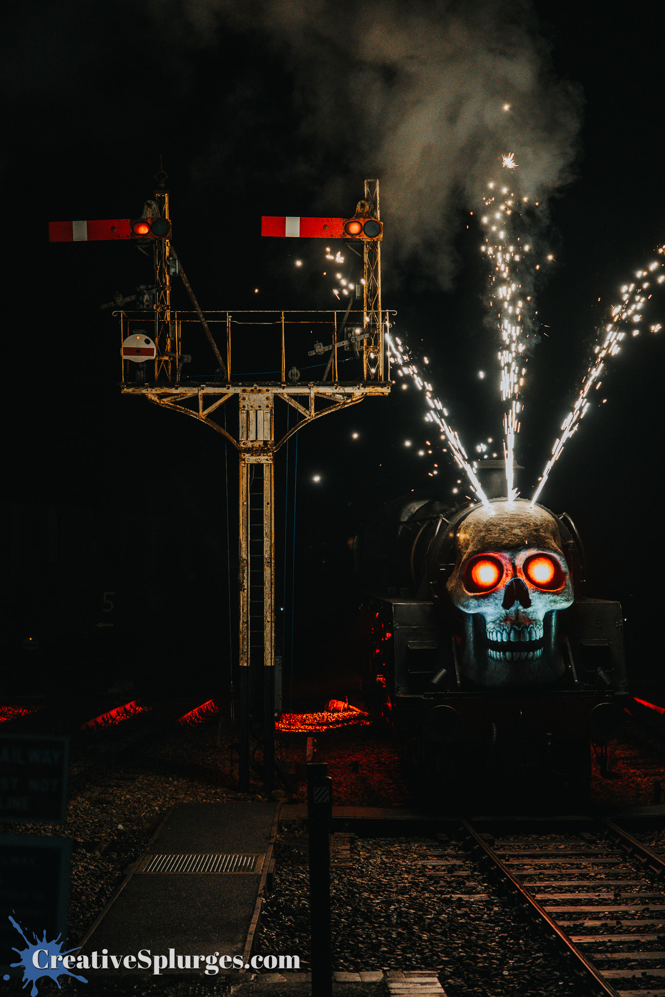 A steam locomotive with a large skull decoration and glowing eyes emits sparks, with railway signals in the background, set against a dark night sky.