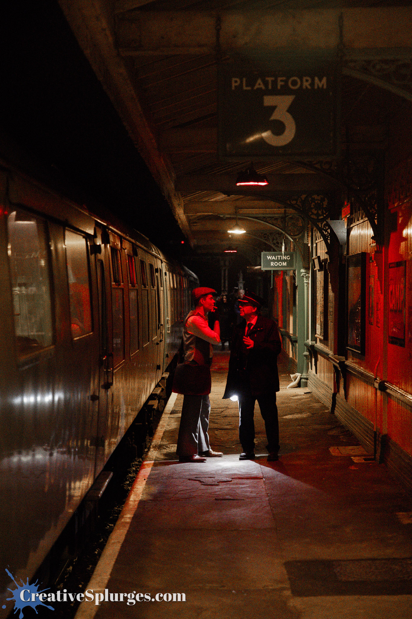 A dimly lit train platform featuring a sign for 'Platform 3'. Two figures, one in a vintage outfit and the other in a uniform, are engaged in conversation near a train.