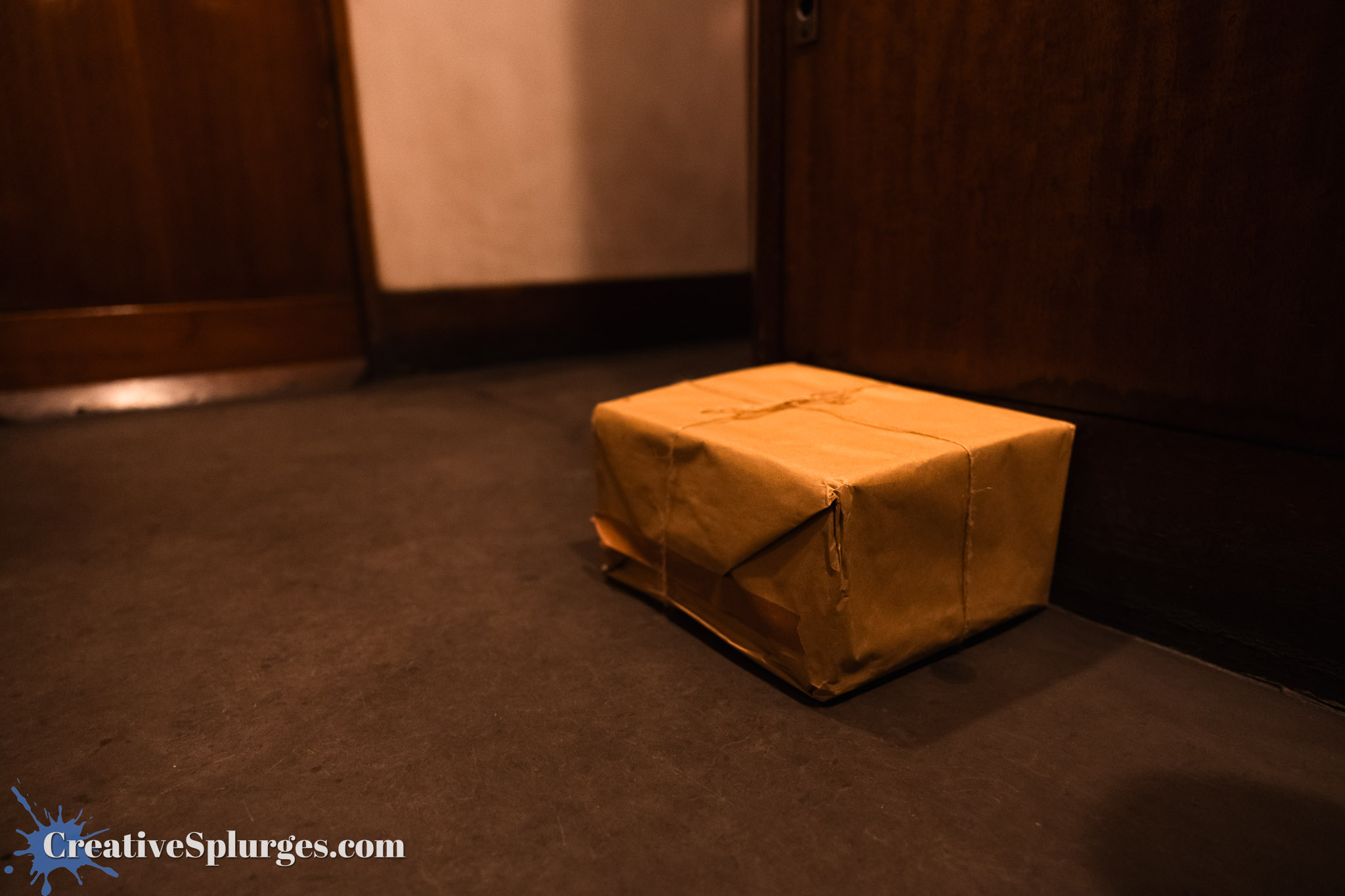 A small, brown package placed on a dark floor near a wooden door.