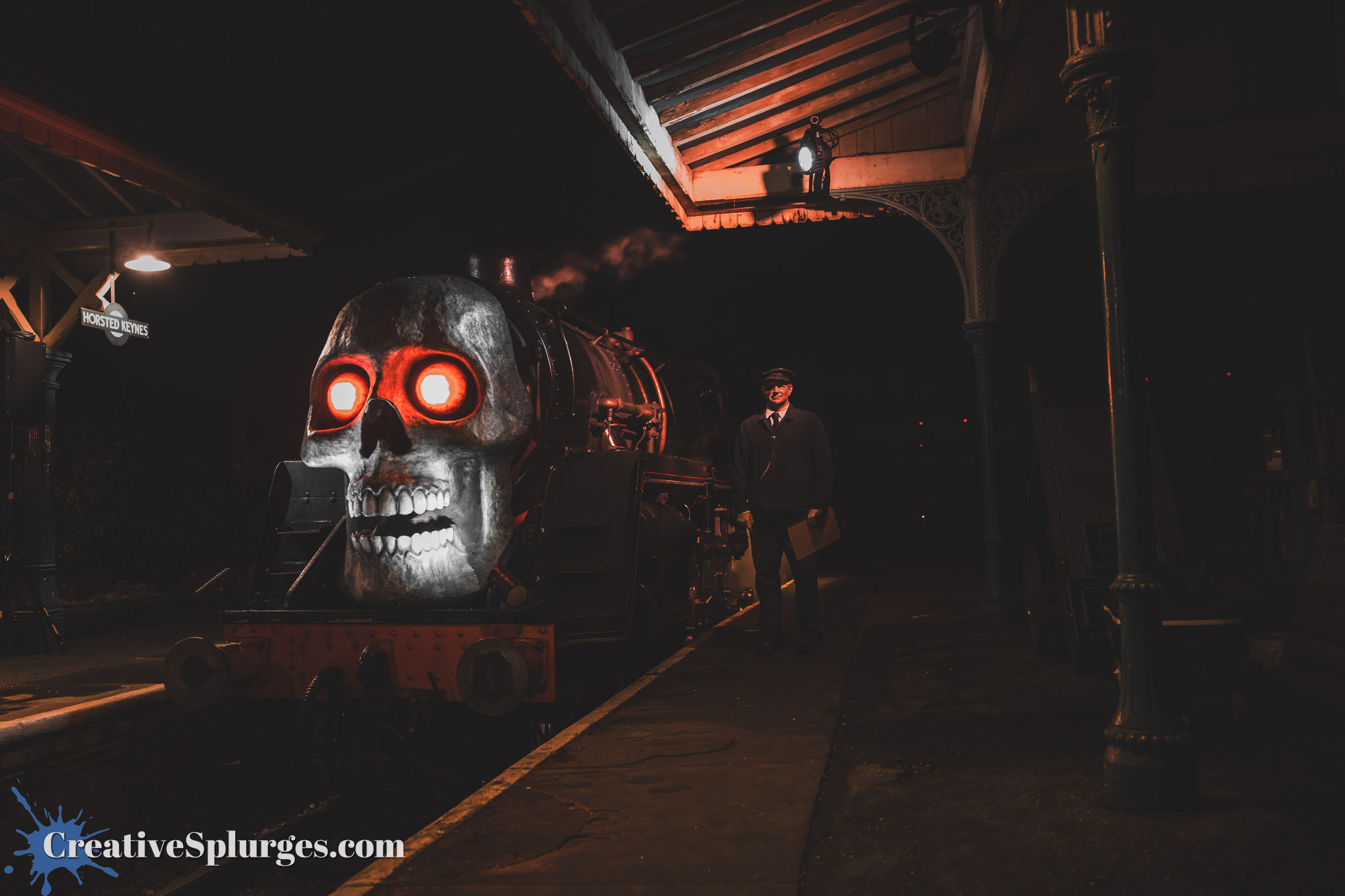 A spooky steam locomotive with a skull design and glowing red eyes, parked at a dimly lit train station. A train conductor in uniform stands nearby, adding to the eerie atmosphere.