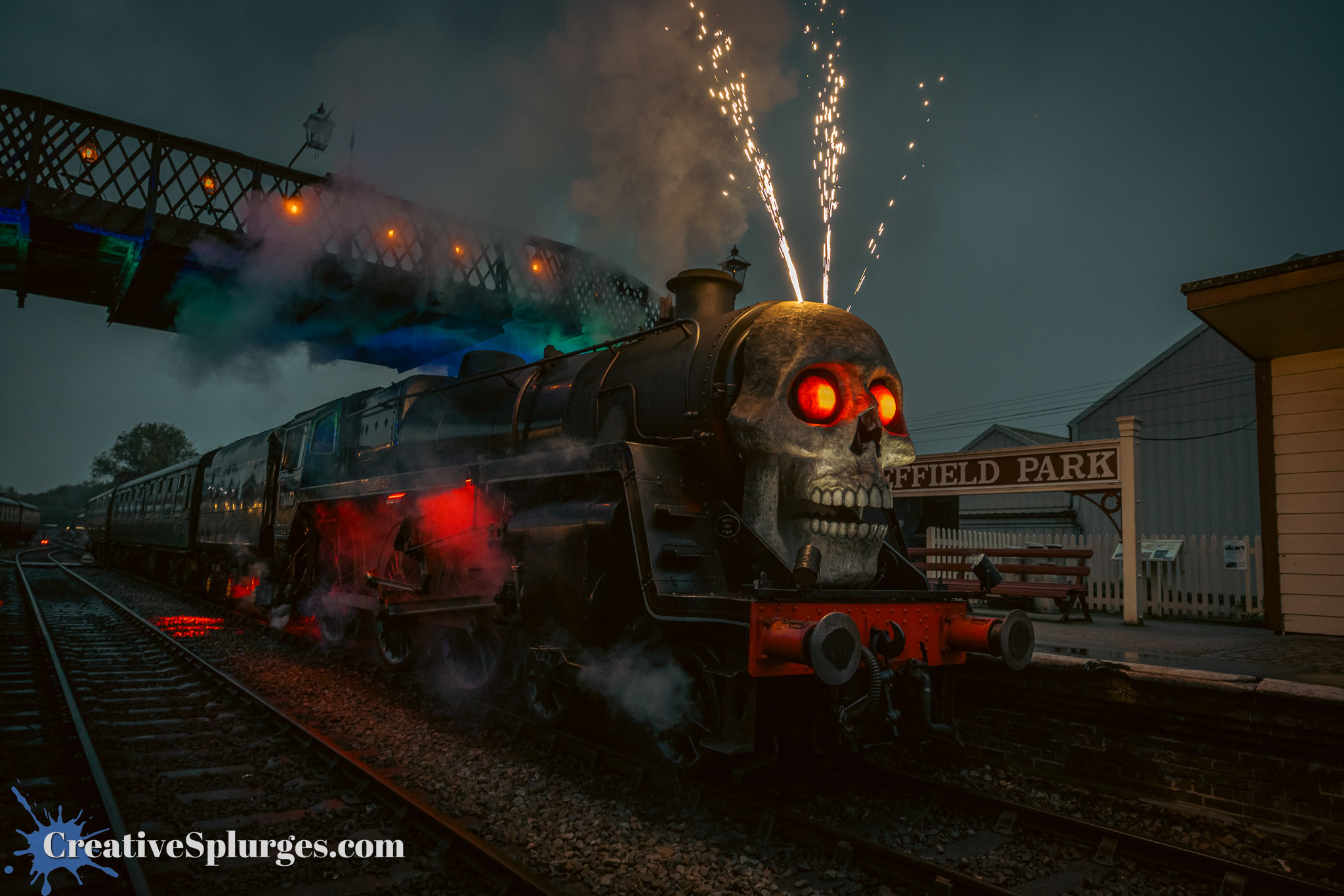 A steam locomotive with a skull-shaped front and glowing red eyes, emitting smoke and sparks, set against a dark sky and a bridge overhead.