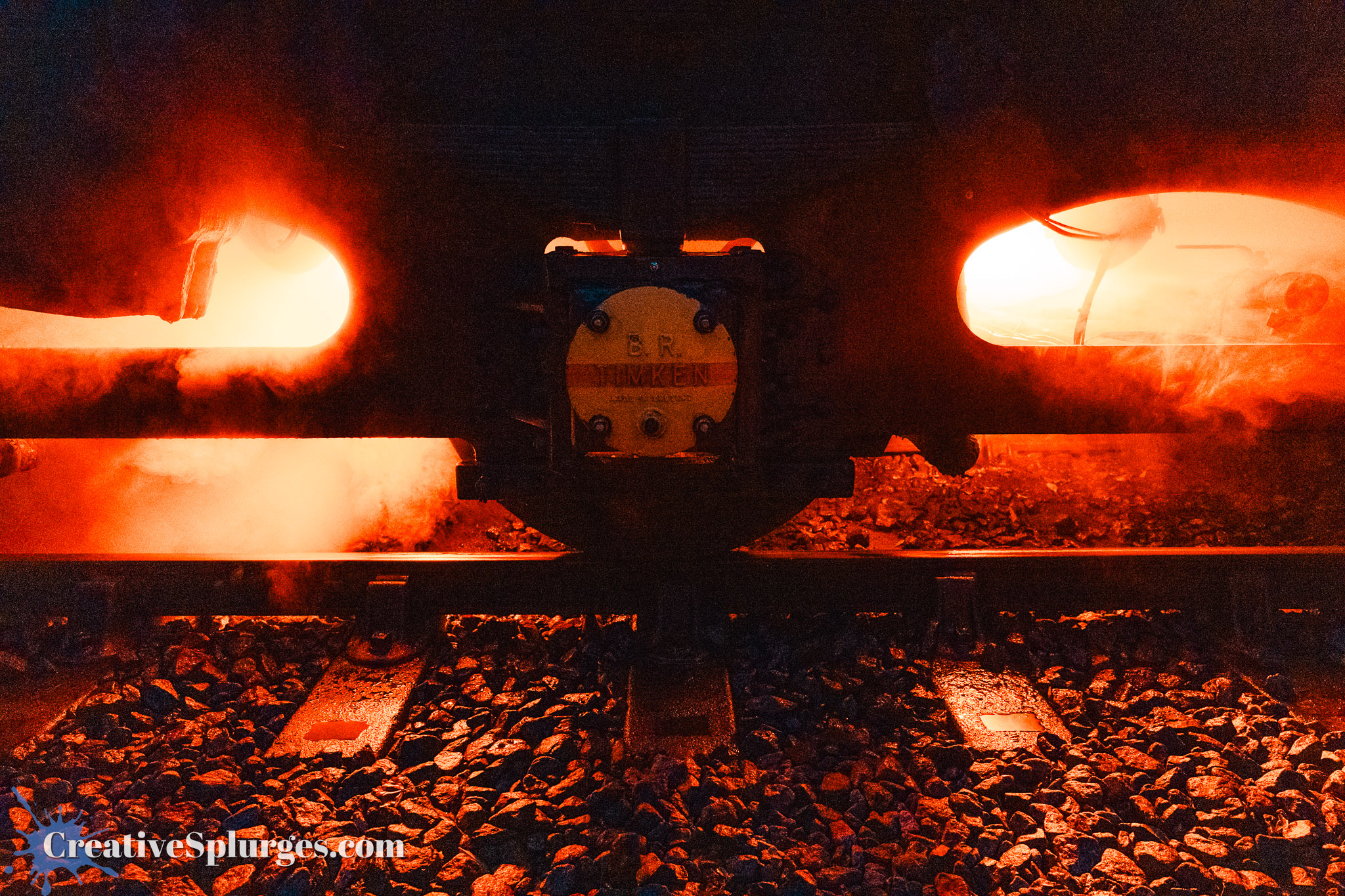 Close-up view of a steam locomotive's wheels and steam emitting from its body, with glowing red lights and smoke effects.