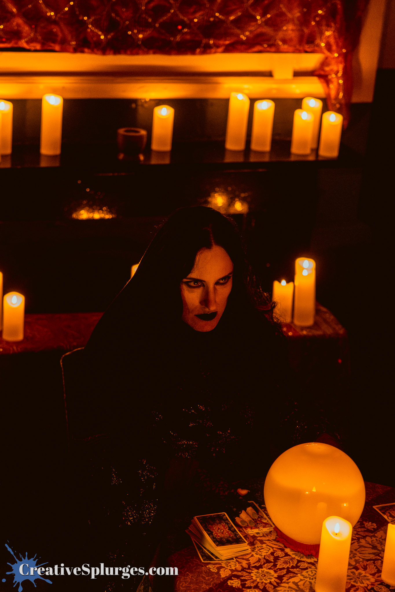 A mysterious figure in a dark cloak sits at a dimly lit table surrounded by candles and a crystal ball, creating an atmosphere of mysticism.
