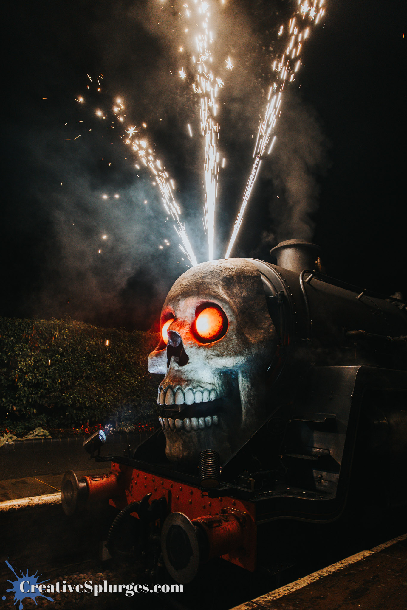 A steam locomotive decorated with a large skull on the front, featuring glowing red eyes and sparks shooting from the top in a nighttime setting.